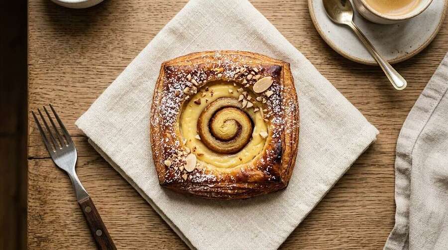A Danish wienerbrød pastry with a depression filled with custard or remonce, light icing on top, on a cream linen napkin